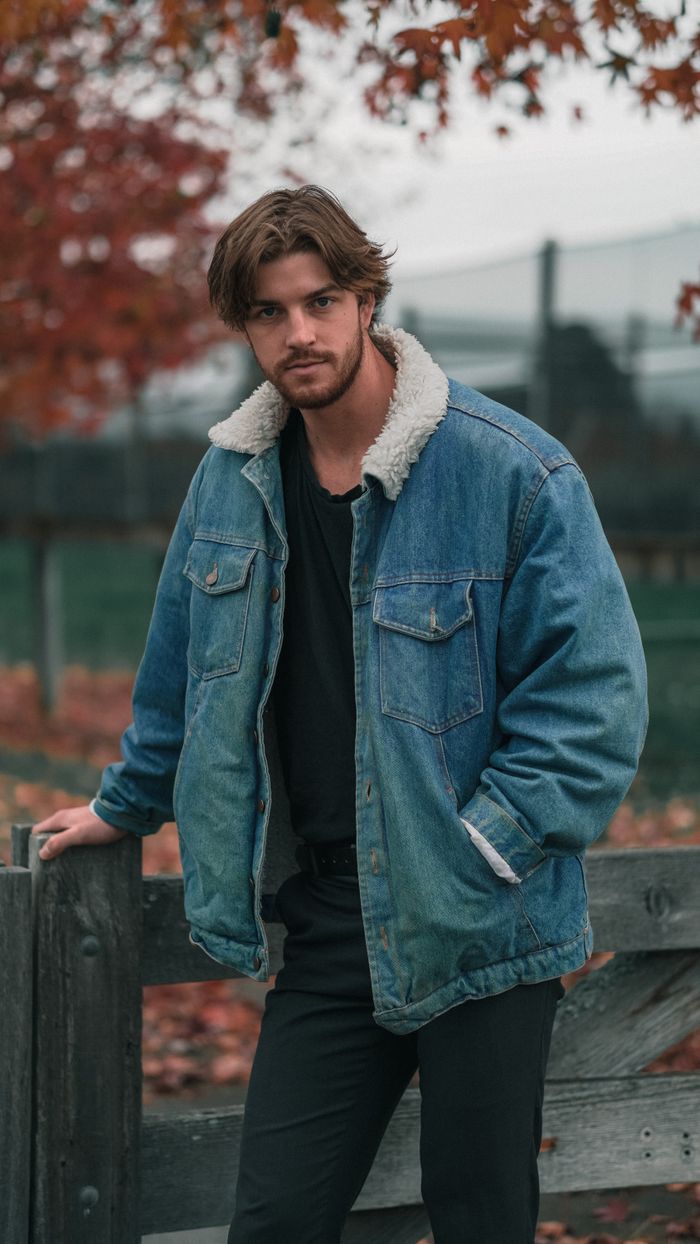why-choose-us A young man wearing a denim jacket stands near a wooden fence surrounded by autumn foliage.